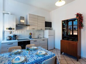 A modern kitchen with white cabinets, a built-in stove, and a dining area set for four with a blue tablecloth. - Lovely apartment for 4 people with WIFI (Albenga)