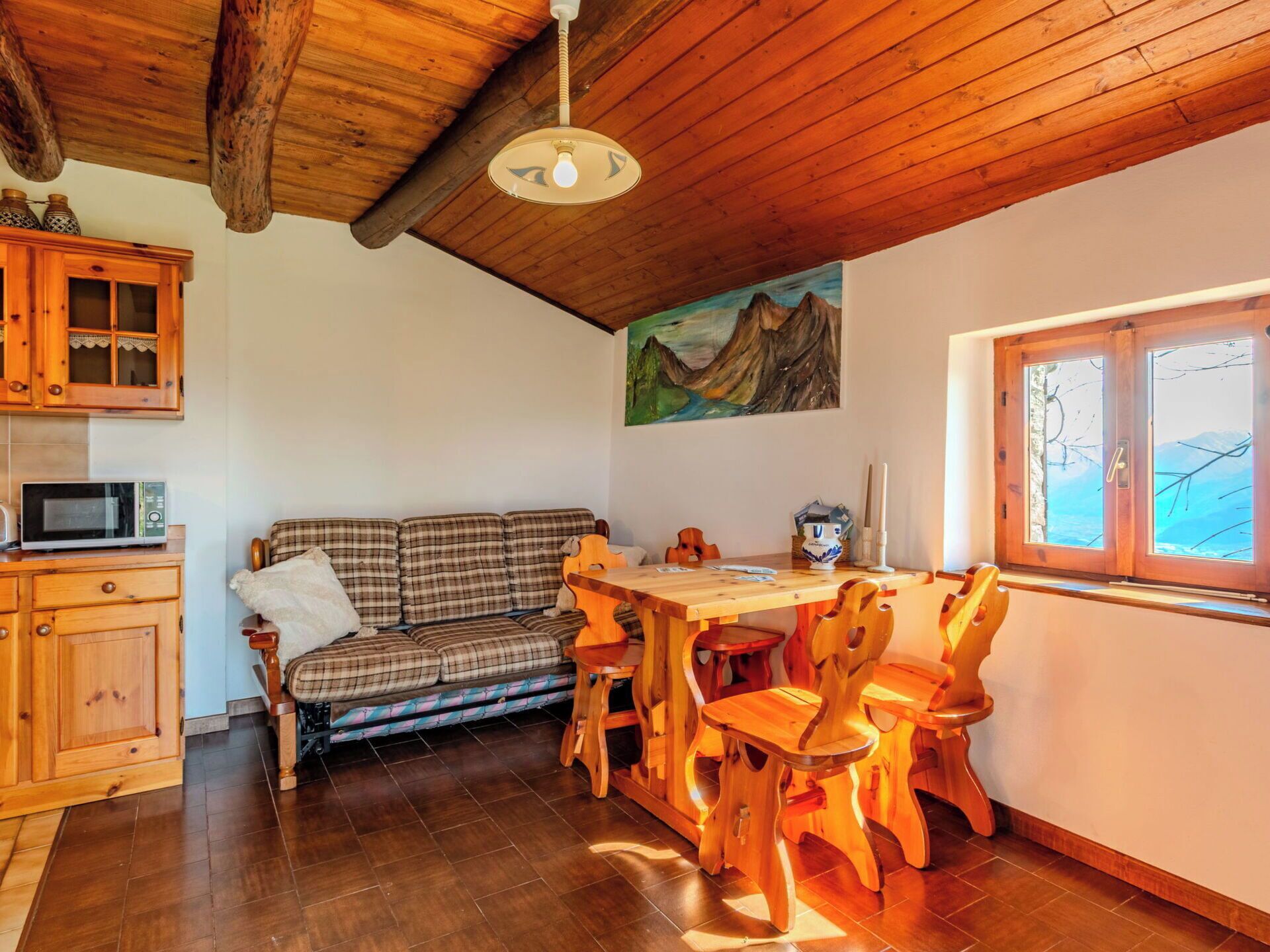 Una habitación acogedora con techo de madera, una mesa de comedor con sillas, un sofá, microondas y una ventana con vistas.