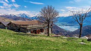 Un edificio de piedra con techo inclinado, una terraza de madera y vistas a un lago y montañas.