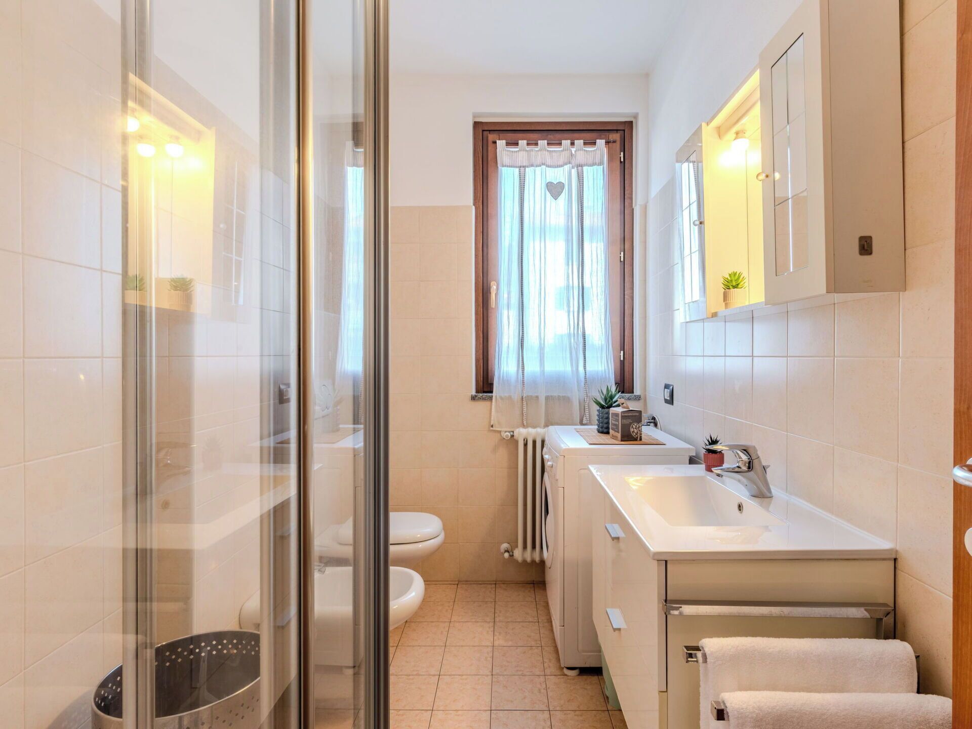A bathroom with a glass shower enclosure, two toilets, a sink, and a mirror.