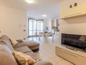 Ein modernes Wohnzimmer mit Sofa, Fernseher und Essbereich mit Stühlen und Tisch.