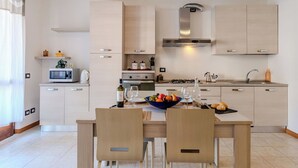 Una cucina moderna con mobili in legno chiaro, un'isola centrale e un'area pranzo con due sedie.