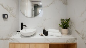 A bathroom with a white marble sink, a round mirror, a black faucet, a potted plant, and a wooden cabinet. - LIV - Comfortable Athens Studio S8-2C (Athens)