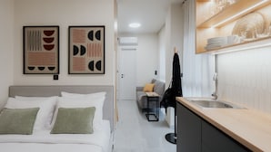 A modern hotel room with a bed, a small sofa, a desk, a kitchen area with a sink, and two framed artworks on the wall. - LIV - Comfortable Athens Studio S8-2C (Athens)