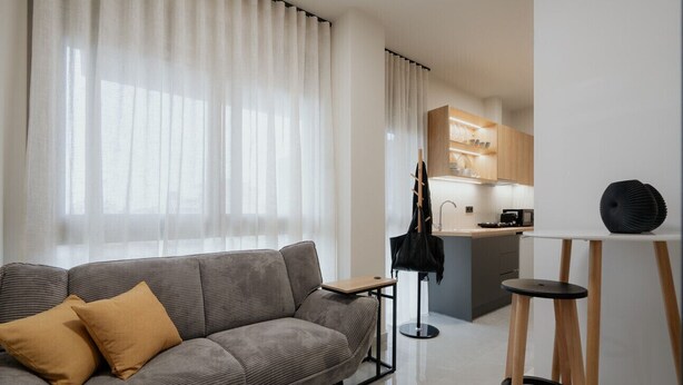 A modern living room with a grey sofa, a small table, and a kitchen area in the background. - LIV - Comfortable Athens Studio S8-2C (Athens)