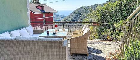 A patio with wicker furniture, a table with a red lamp, and a view of a red building and hills.