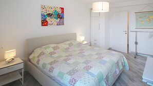 Ein Schlafzimmer mit Bett, Nachttisch, Lampe, Kleiderschrank und einer Weltkarte an der Wand.