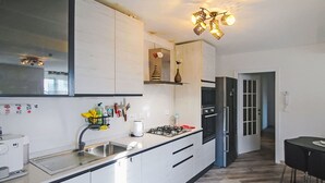Eine moderne Küche mit weißen Schränken, einem Gasherd, einem Kühlschrank und einem Essbereich mit Tisch und Stühlen.