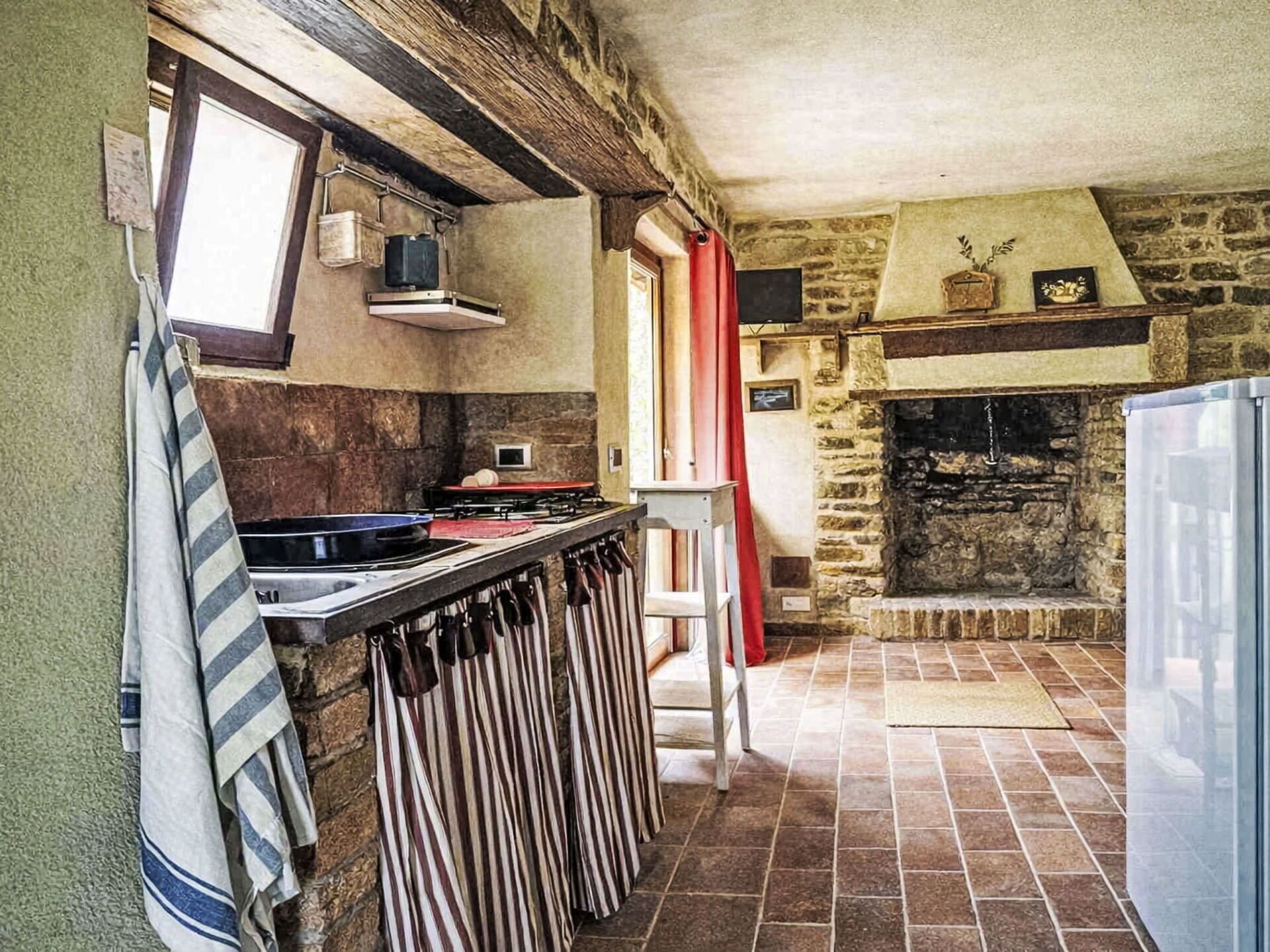 A rustic kitchen with a stone wall, a fireplace, and a tiled floor.