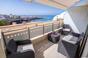 Ein Balkon mit Korbmöbeln, einem Blumentopf und Blick auf das Meer und die Gebäude.