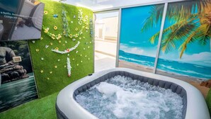 A hot tub with a view of the ocean, surrounded by artificial grass and decorative flowers.