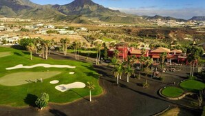 A golf course with sand bunkers, palm trees, and a mountainous backdrop.