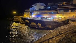 A waterfront building with a bridge, reflecting lights on the water.