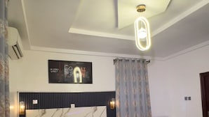 A modern bedroom with a large bed, a headboard with a marble pattern, a bedside table, and a ceiling light fixture. - SIX DIAMOND HOTEL OPEBI (Lagos)