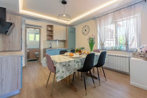 Una cocina moderna con comedor, armarios de madera, un reloj y una ventana con cortinas.