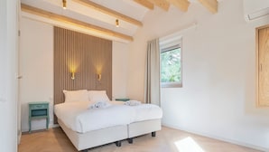 A bedroom with a bed, a nightstand, a window, and a wooden ceiling beam. - Studio Linde - in the serene woods of Aerdenhout (Aerdenhout)