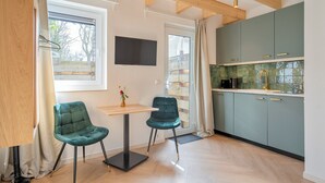 A modern kitchen with teal cabinets, a wooden ceiling, and a dining area with two teal chairs. - Studio Linde - in the serene woods of Aerdenhout (Aerdenhout)