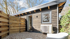 A wooden cabin with a sliding door, a window, and an air conditioning unit. - Studio Linde - in the serene woods of Aerdenhout (Aerdenhout)