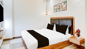 A modern hotel room with a large bed, a bedside table with a vase of flowers, and a wall-mounted light fixture. - Classic The Century Plaza Hotel (Varanasi)