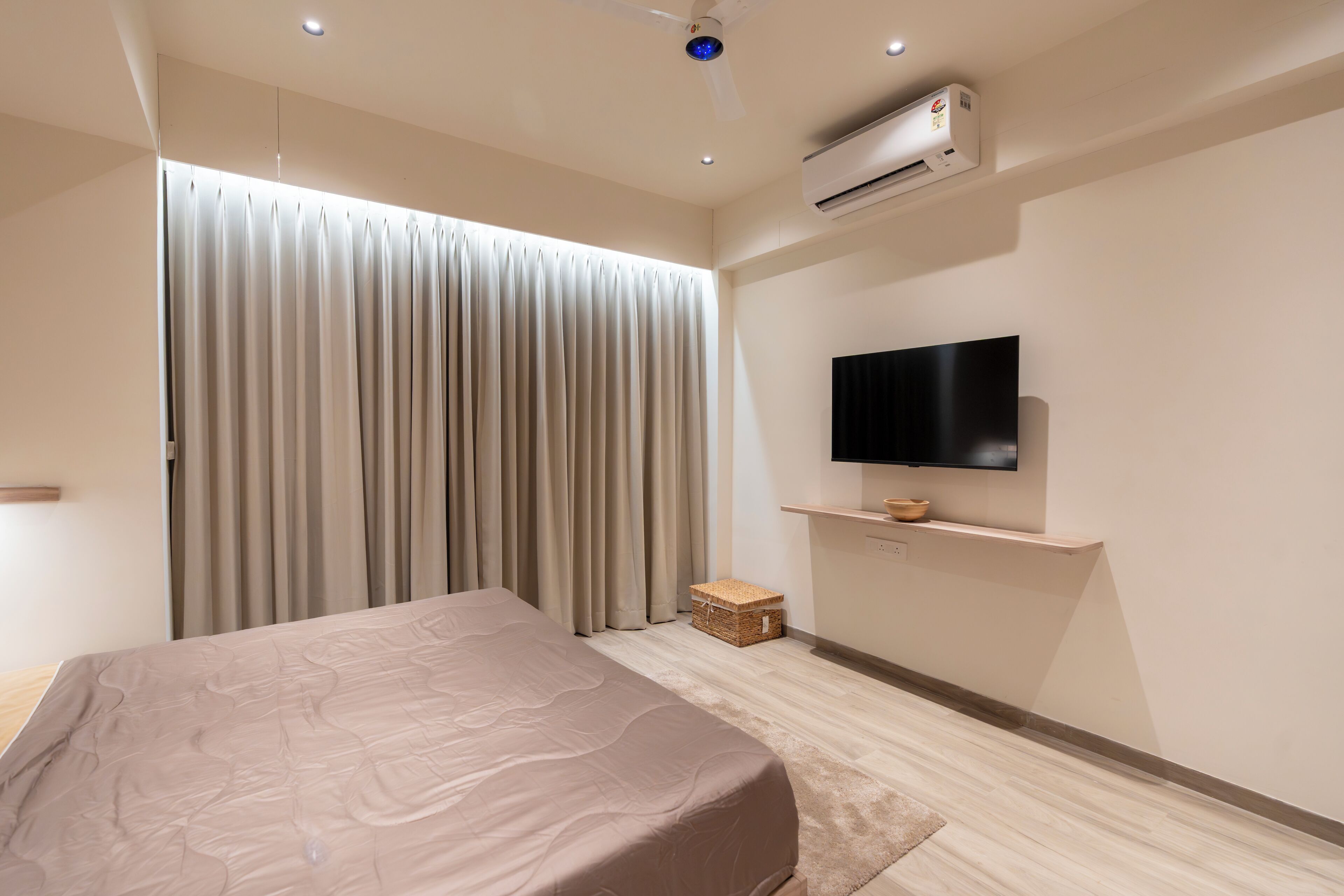 A modern bedroom with a bed, a flat-screen TV, an air conditioner, and a large window with curtains.