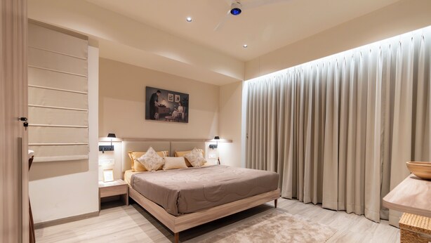 Un dormitorio con cama, mesitas de noche, un cuadro, ventilador de techo y una ventana con cortinas.