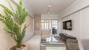A modern living room with a sofa, a glass coffee table, a potted plant, and a flat-screen TV mounted on the wall. - Sol & Sage (Cape Town)