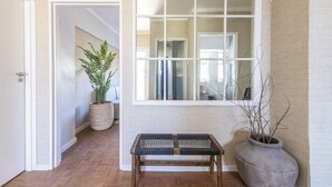 A hallway with a wooden bench, a large window, a potted plant, and a door leading to another room. - Sol & Sage (Cape Town)