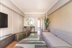 A modern living room with a sofa, ottoman, TV, and a large mirror. - Sol & Sage (Cape Town)