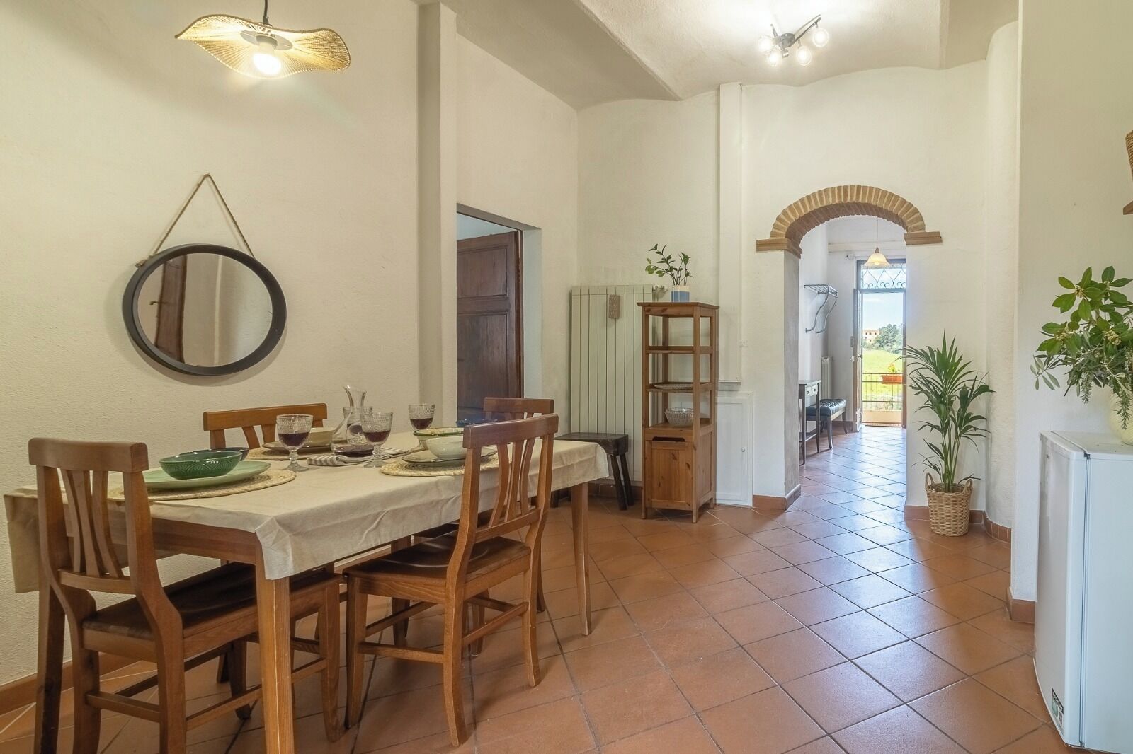 A dining area with a table set for four, chairs, a wooden sideboard, a mirror, and a potted plant.