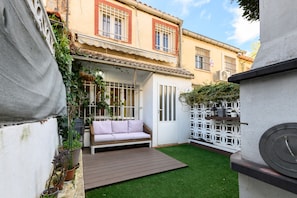 A courtyard with a wooden deck, a white sofa, and a small garden area.