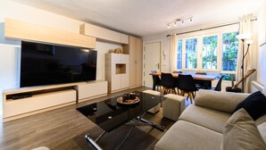 A modern living room with a flat-screen TV, a glass coffee table, a sofa, a dining area with chairs, and a large window with curtains. - (SAB52) Spacious 3-bedroom villa with terrace (Madrid)