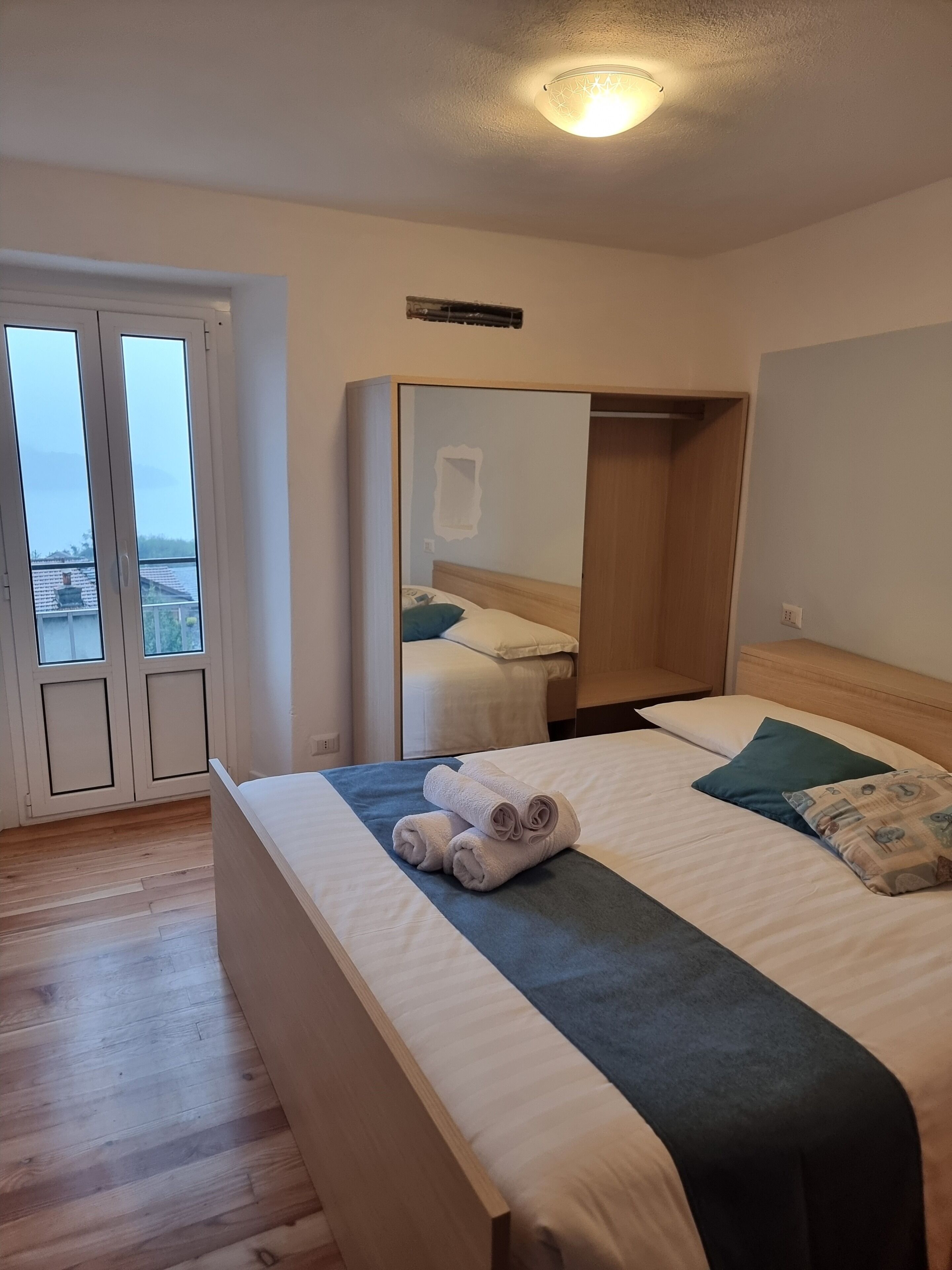 Een hotelkamer met een bed, een spiegel, een kledingkast en uitzicht door een glazen deur.