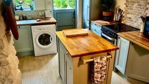 Eine kleine Küche mit Waschmaschine, einer Holz Arbeitsplatte und Blick auf Grünfläche.
