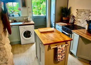 Une cuisine compacte équipée d’un lave-linge, dotée d’un plan de travail en bois et offrant une vue sur la verdure environnante.