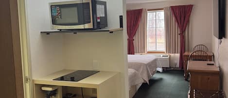 Une chambre d’hôtel de taille réduite, équipée d’une kitchenette, d’un lit, d’un bureau et d’une télévision.