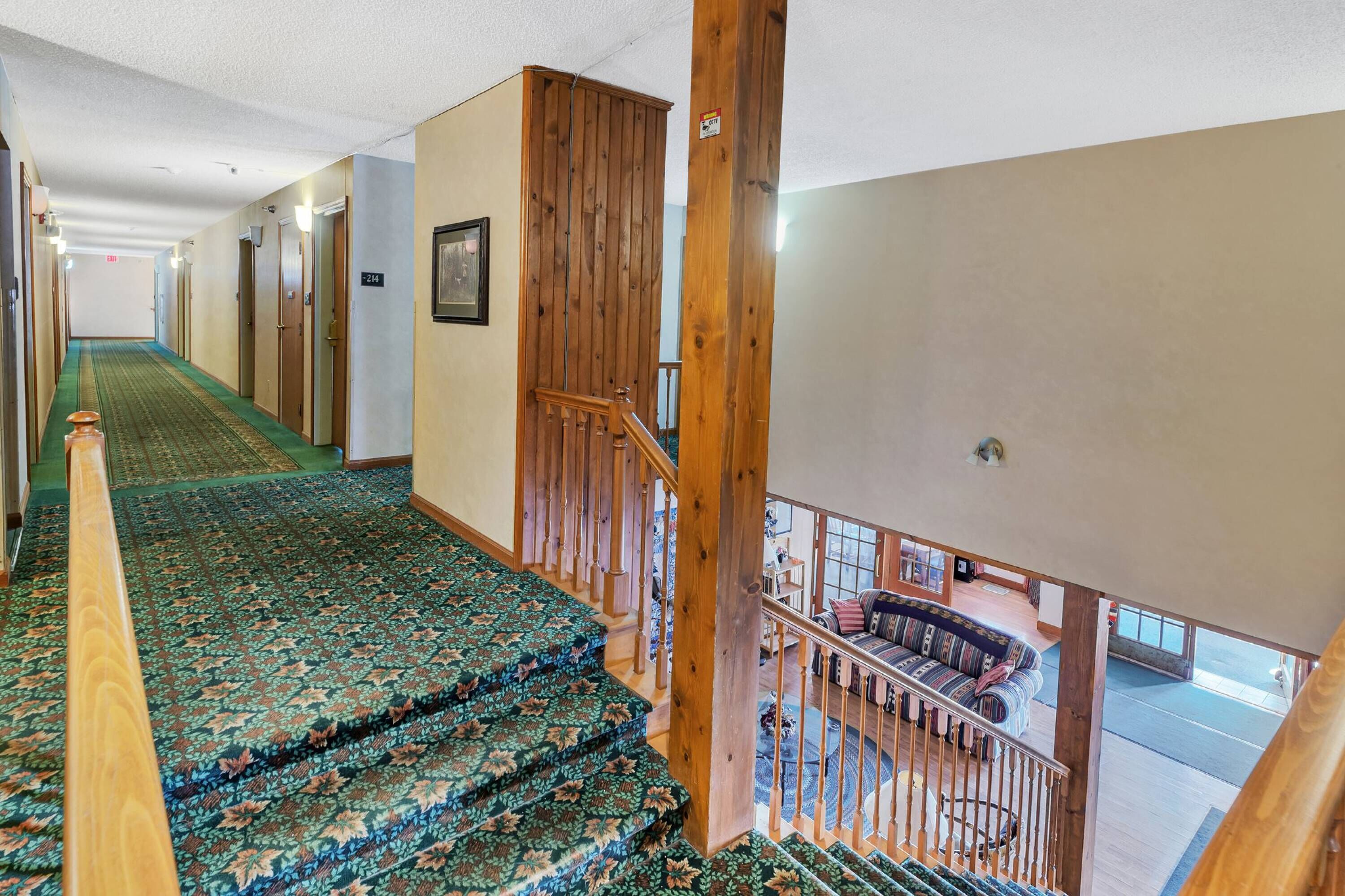 Un couloir d’hôtel avec des escaliers recouverts de moquette, des rampes en bois et une vue sur un espace détente comprenant un canapé et une table basse.