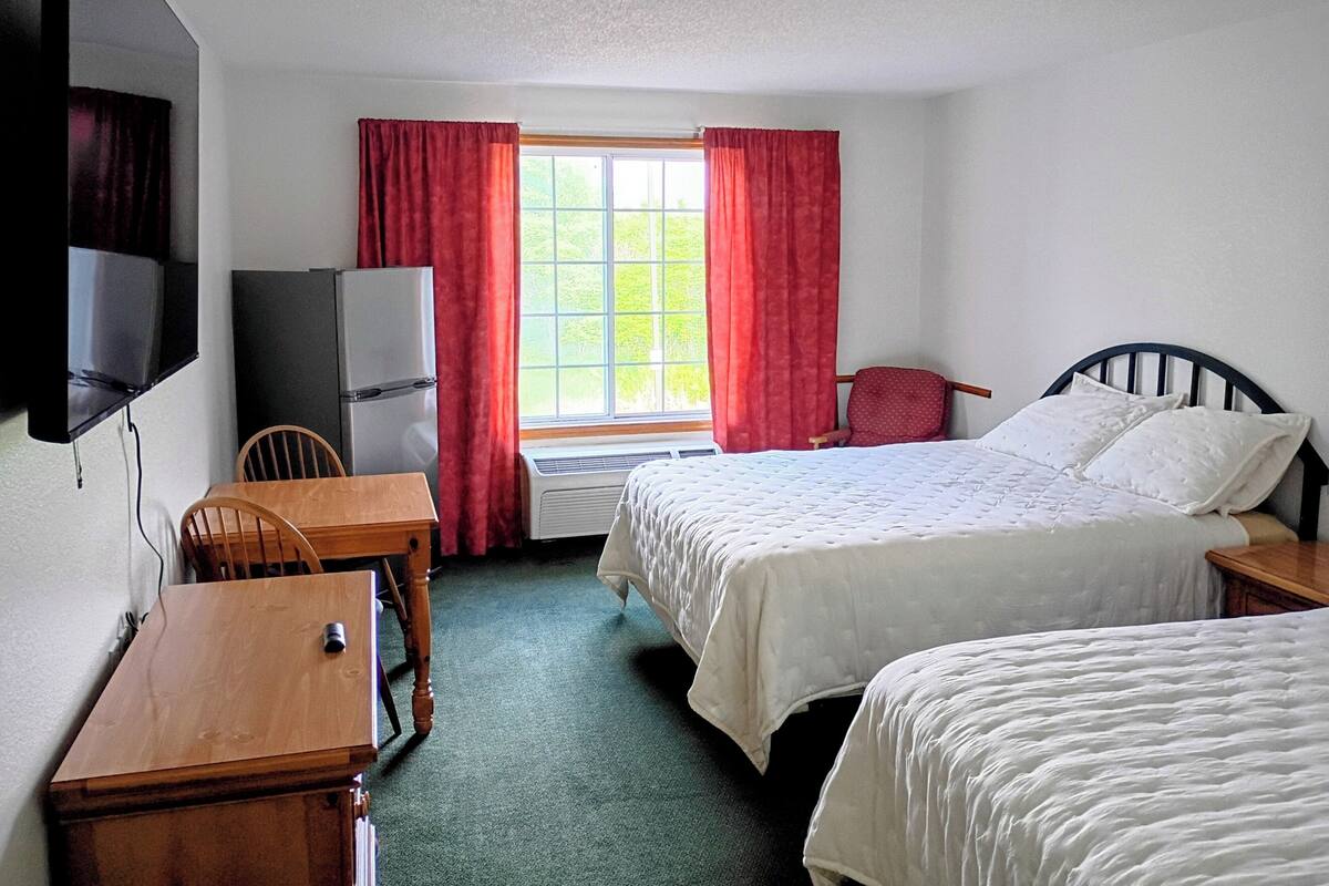 A hotel room with two beds, a TV, a desk, a chair, and a window with curtains.