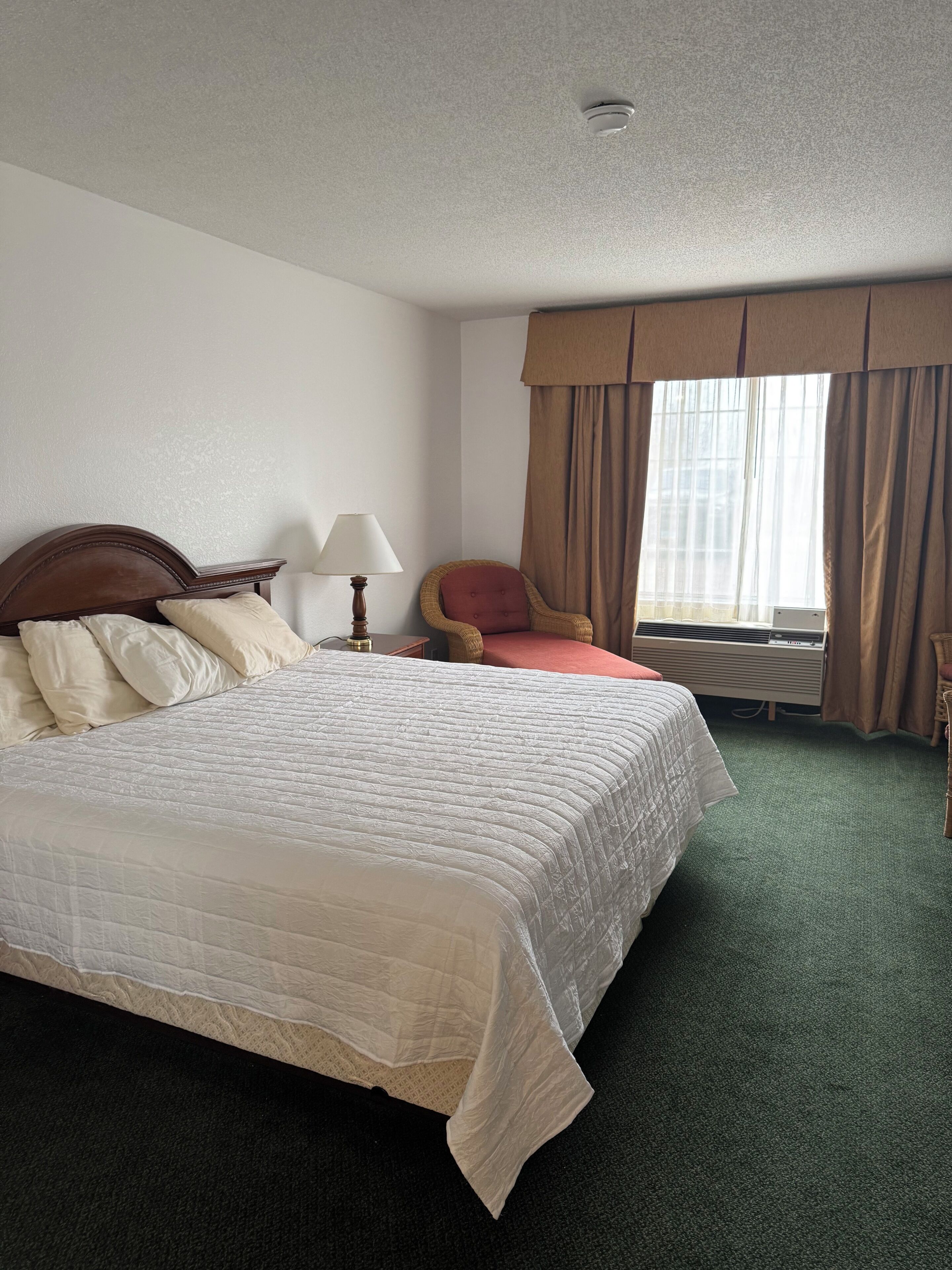 A hotel room with a large bed, a chair, a lamp, and a window with curtains.