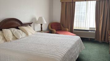 A hotel room with a large bed, a chair, a lamp, and a window with curtains.