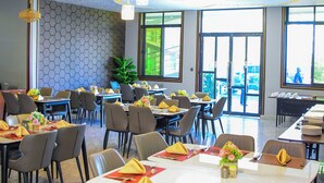 Un comedor moderno con mesas dispuestas para varios invitados, techo decorativo y ventanas amplias que dejan entrar luz natural.