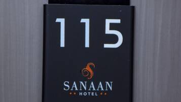 Un letrero negro con el número 115 y el nombre 'Sanaam Hotel' sobre una pared gris.