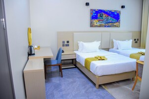 Habitación de hotel con dos camas, un escritorio, una silla, una cafetera y un cuadro en la pared.