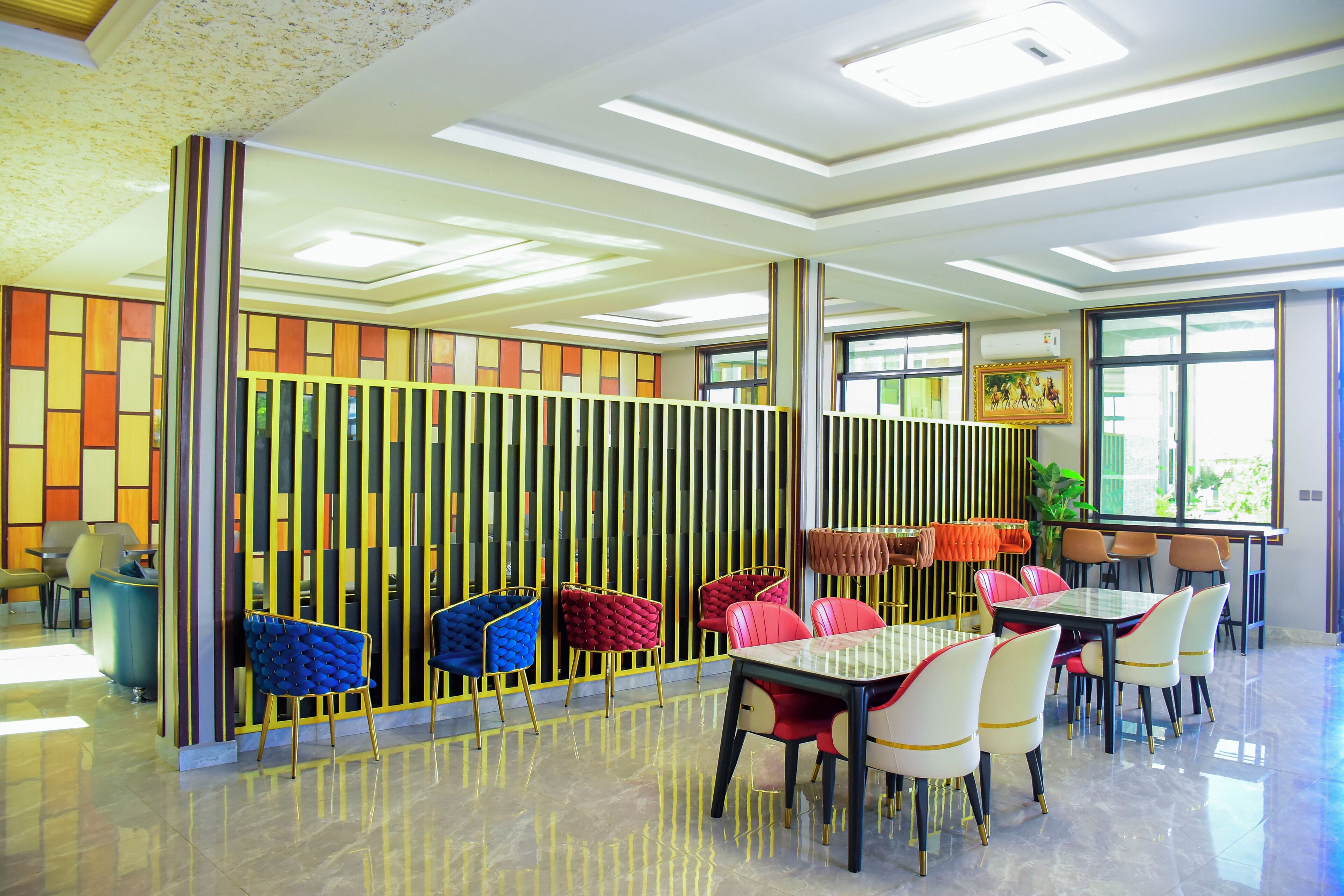 A modern dining area with a high ceiling, a glass partition with colorful panels, and a variety of chairs and tables.