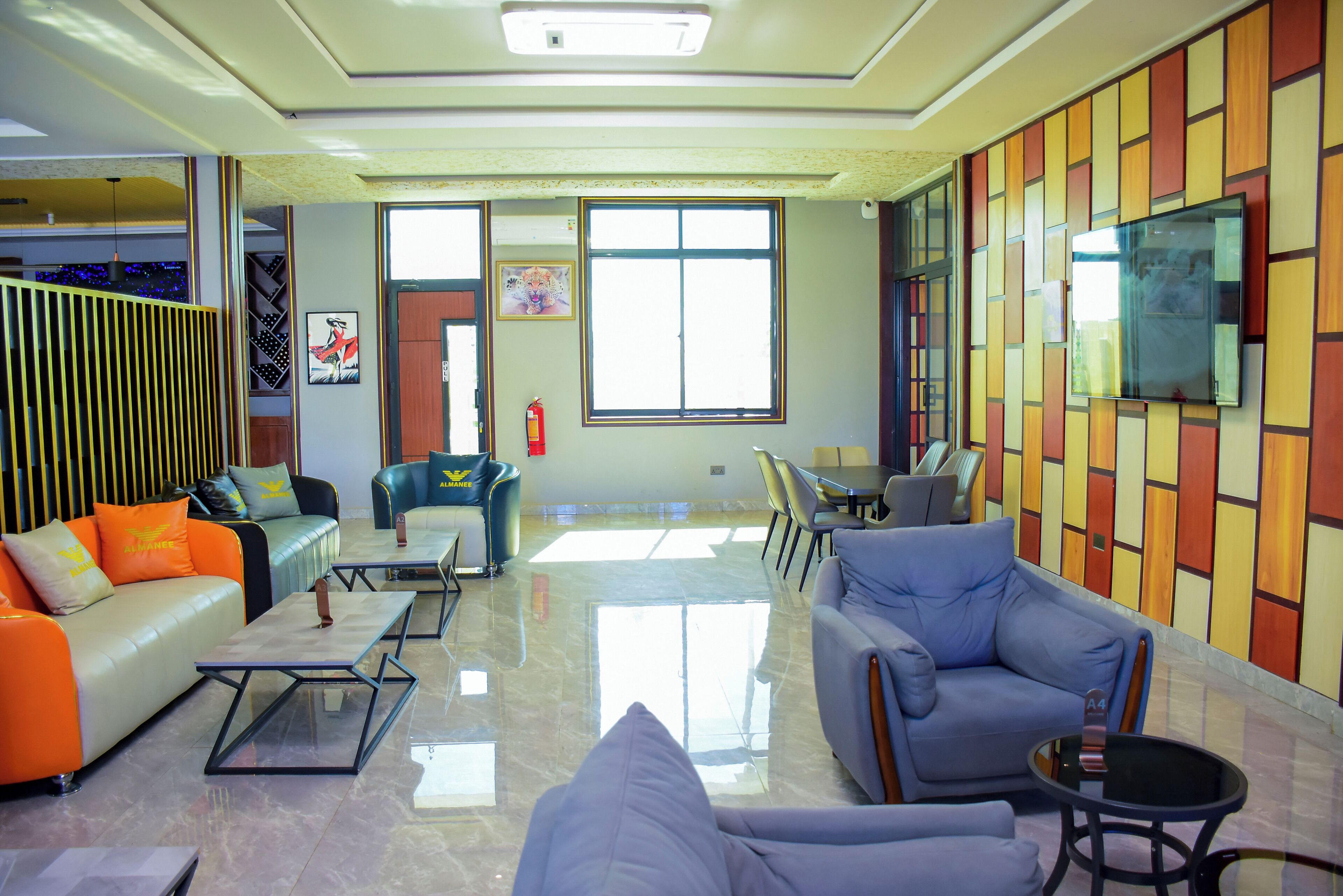 A modern hotel lobby with seating areas, a flat-screen TV, and a fire extinguisher.