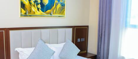Habitación de hotel con una cama grande, un cuadro en la pared, una mesita de noche y una silla.