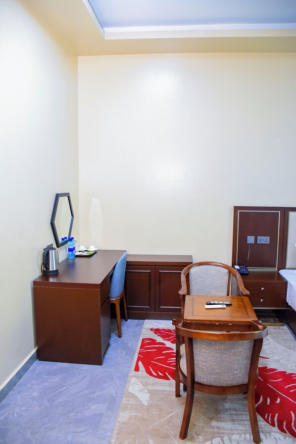 A hotel room with a wooden desk, a chair, a bed, a wardrobe, and a red patterned rug. - SANAAN HOTEL DODOMA (Dodoma)