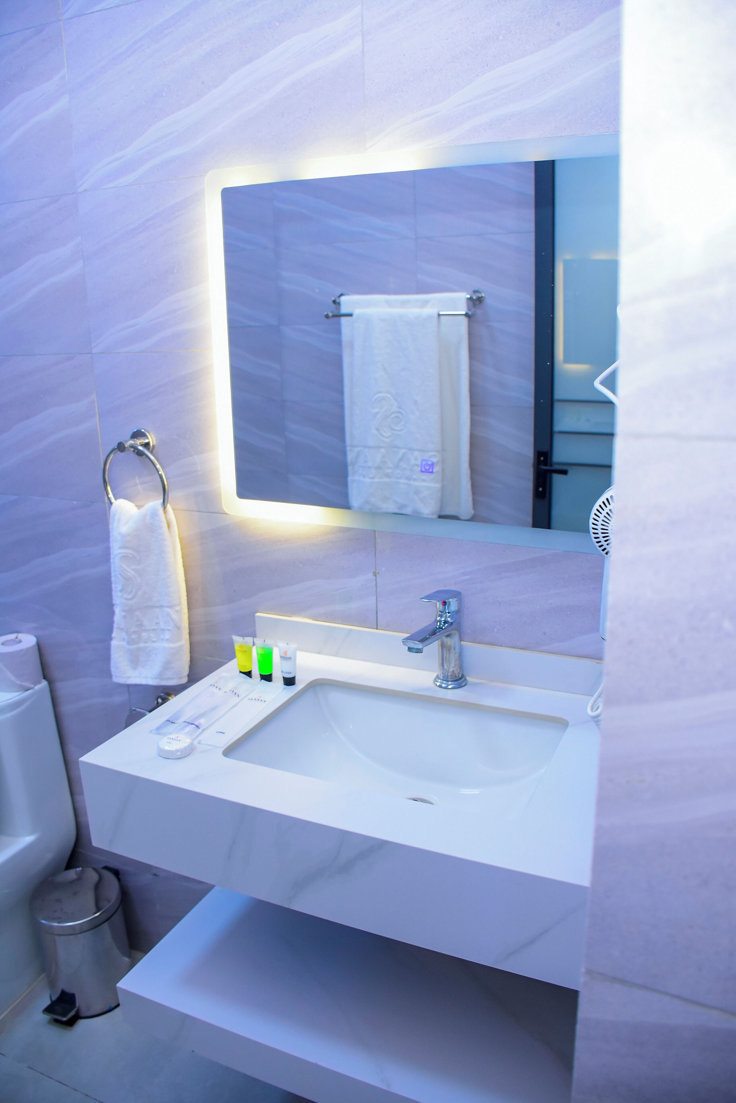 A bathroom with a white sink, a mirror, a towel rack, and a trash bin.
