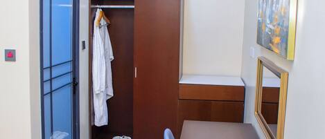 A small room with a wardrobe, a bench, a table, a mirror, and a painting on the wall.