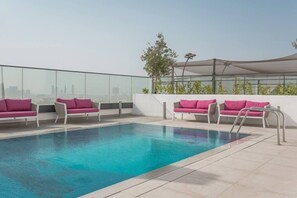 A rooftop pool area with a clear view of the city skyline, equipped with multiple lounge chairs and a covered seating area. - FIRST CLASS | 1BR | Vibrant Modern Living (JVC)