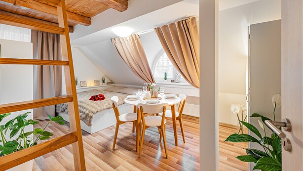 A dining area with a round table, chairs, and a wooden ladder. - Karlsbad Apartments (Karlovy Vary)